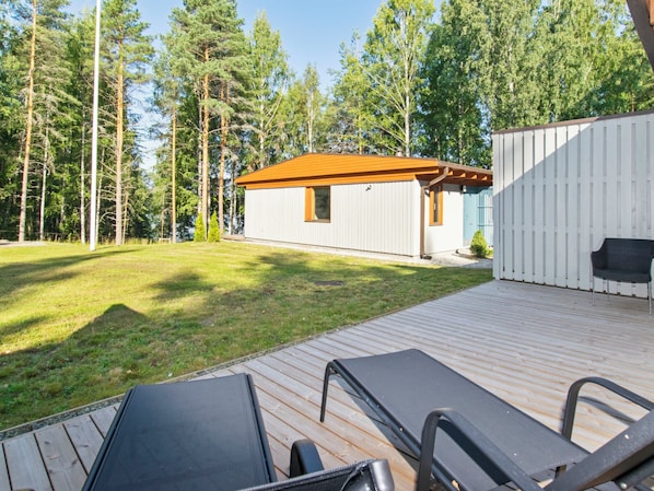A wooden deck with two lounge chairs, a small building with a red roof, and a white fence.