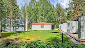 A cabin with a red roof, surrounded by a wooden deck and a fenced yard.