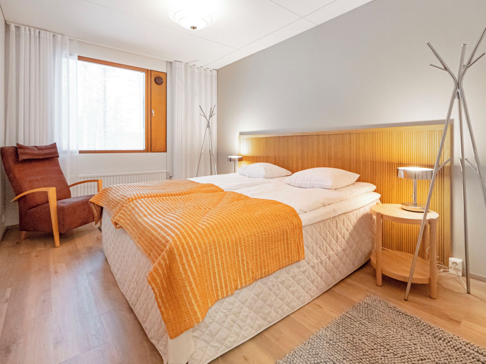 Hotellihuone, jossa on sänky, tuoli, yöpöytä ja lamppu.