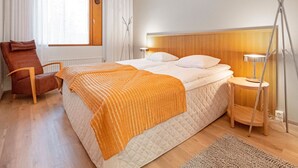 Una habitación de hotel moderna con una cama grande, una silla, una mesita de noche con lámpara y una lámpara de pie.
