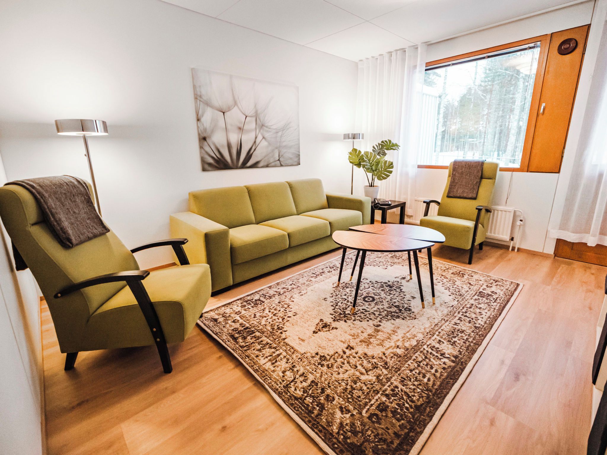 A modern living room with a sofa, two armchairs, a coffee table, a floor lamp, a potted plant, and a large window.