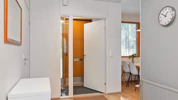 A hallway with a white door leading to a room with a wooden door, a dining area with chairs, and a wall clock.