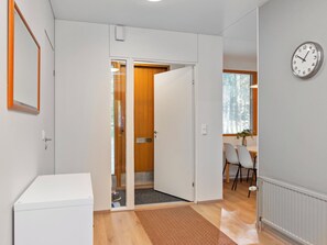 Corredor com uma porta branca que dá para um quarto com porta de madeira, sala de jantar com cadeiras e um relógio na parede.