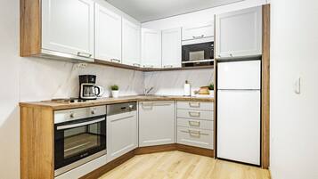 Cozinha compacta com armários brancos, forno embutido, cafeteira e geladeira.