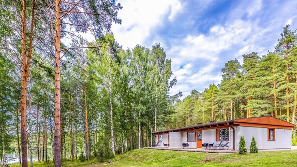 Une cabane dotée d’une terrasse en bois et de meubles d’extérieur, entourée de grands pins.