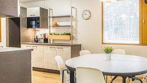 Une cuisine moderne avec une table à manger ronde et des chaises, une horloge et une fenêtre avec des stores.
