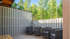 Une terrasse en bois, agrémentée de chaises et d’une table en osier, entourée d’une clôture blanche et d’arbres.