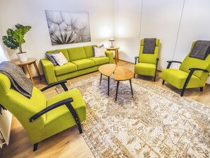 Ein modernes Wohnzimmer mit einem grünen Sofa, zwei Sesseln, einem Couchtisch und einem gemusterten Teppich.