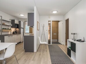 Uma cozinha moderna com armários brancos, uma área de jantar com mesa e cadeiras brancas, e um corredor com porta que dá para outro cômodo.