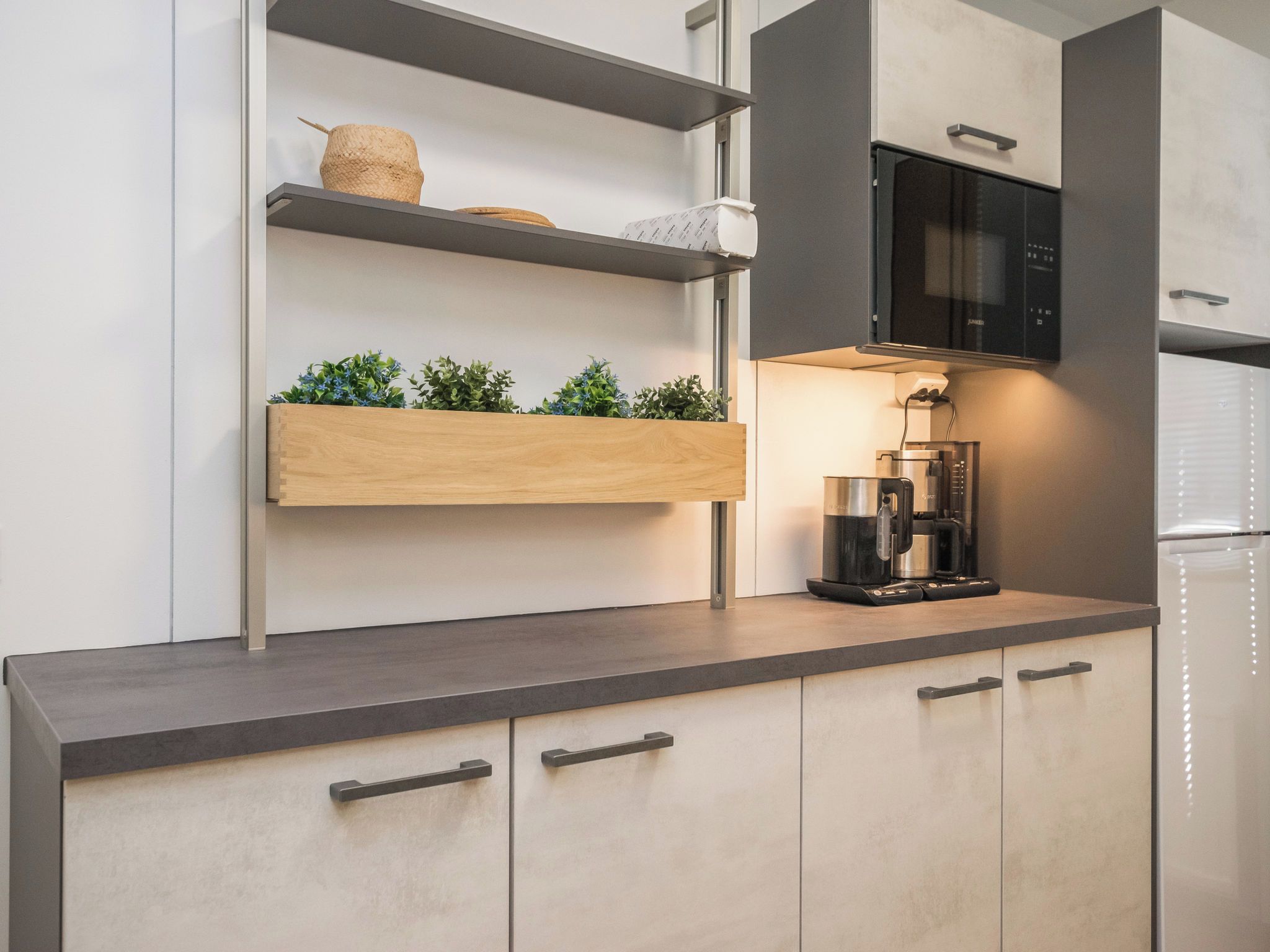 A modern kitchen with a built-in microwave, a coffee maker, and wooden shelves with plants.