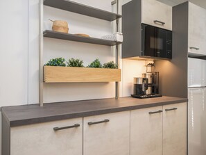 A modern kitchen with a built-in microwave, a coffee maker, and wooden shelves with plants.
