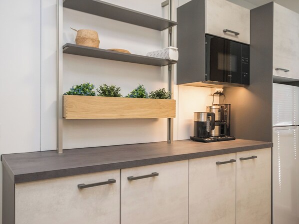 Una cocina moderna con microondas integrado, cafetera y repisas de madera con plantas.