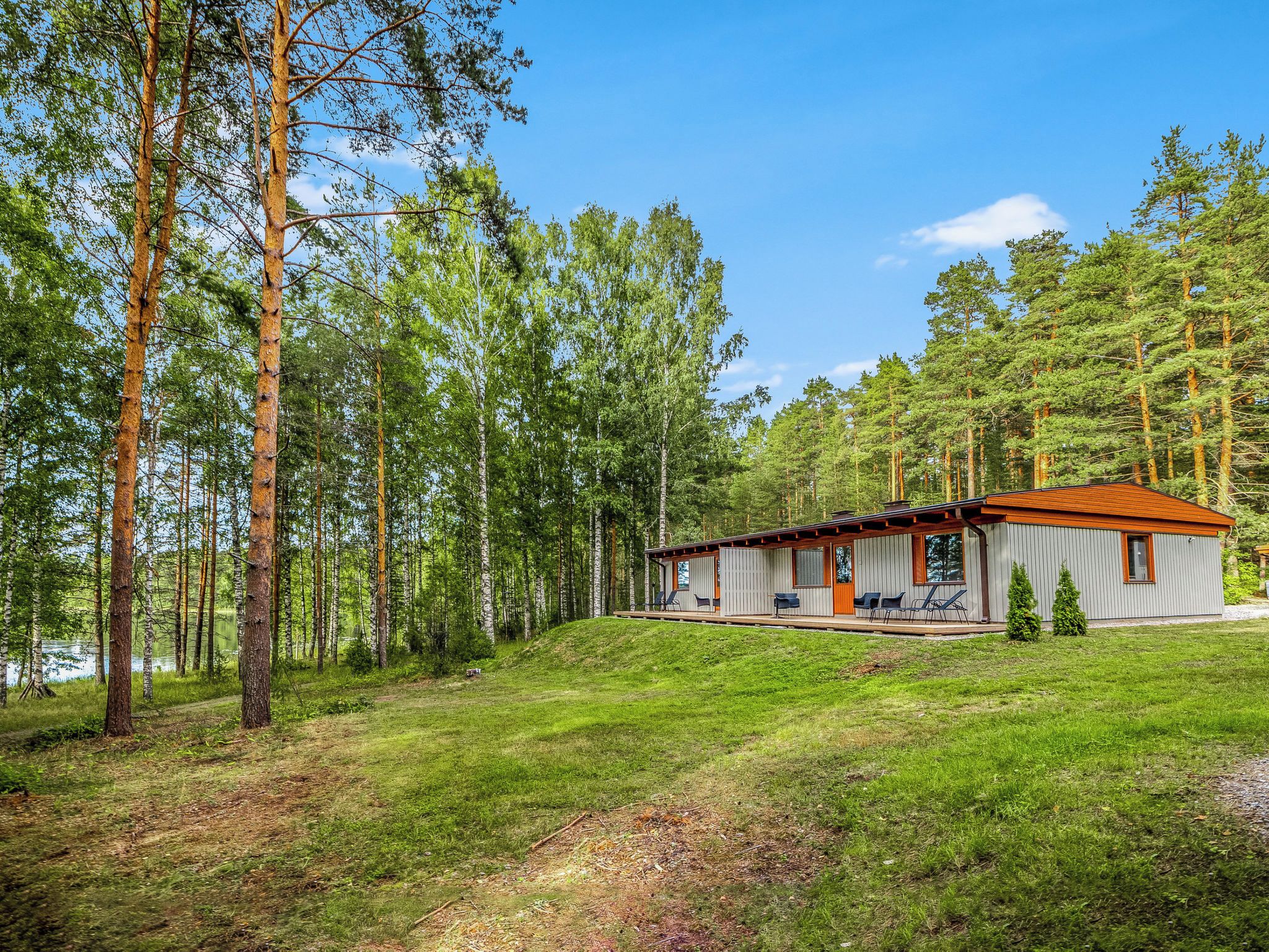 A cabin with a deck and outdoor seating, surrounded by a forest and a lake.