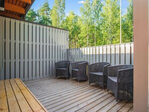 Ulkoterassi, jossa on puinen pöytä ja punottuista materiaaleista valmistetut tuolit. Terassia ympäröi valkoinen aita ja puita.