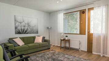 A modern living room with a green sofa, a patterned rug, a floor lamp, and a window with blinds.