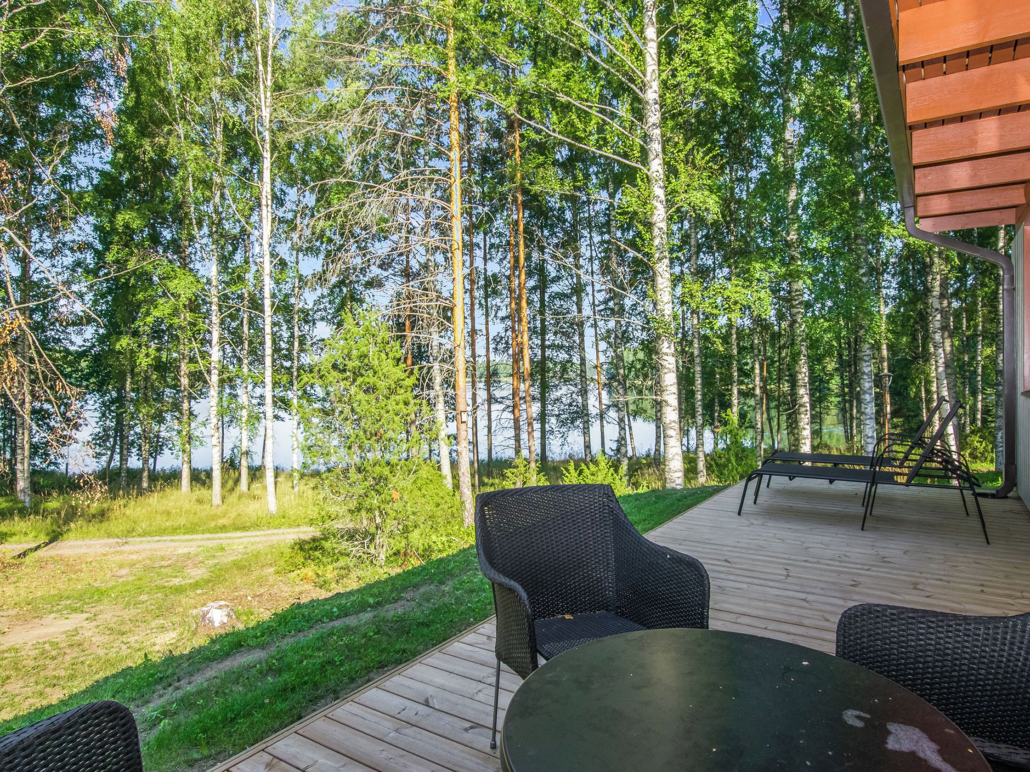 An outdoor deck with a table and chairs, surrounded by a forest and a lake.