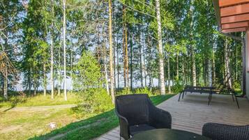 An outdoor deck with a table and chairs, surrounded by a forest and a lake.