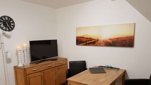 Ett modernt vardagsrum med ett TV-bord i trä, en platt-TV, ett matbord och en stor landskapsmålning på väggen.