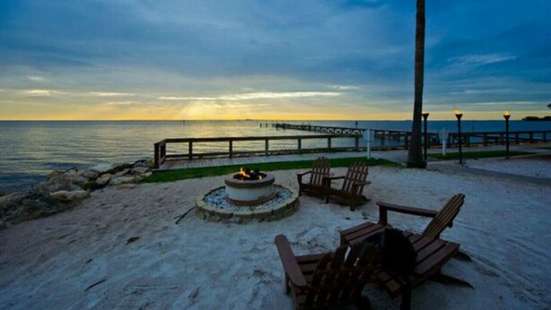 A beachside patio with a fire pit, chairs, and a view of the ocean at sunset.