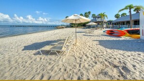 A beach with sun loungers, a beach umbrella, and kayaks.