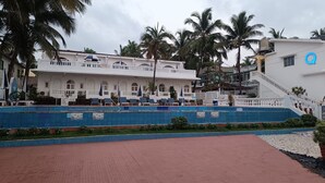 A hotel with a pool area, palm trees, and a staircase leading to the entrance. - Qees Empire Beachfront Resort (Calangute)