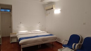 A bedroom with a double bed, a nightstand, a chair, and an air conditioning unit. - Qees Empire Beachfront Resort (Calangute)