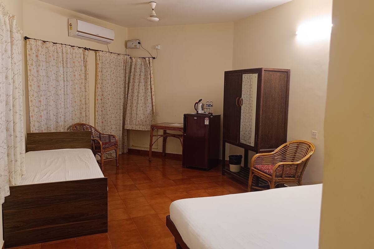A hotel room with two beds, a small table, a refrigerator, and a wardrobe.