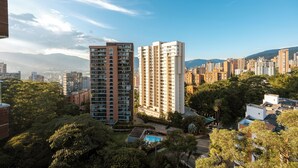 A high-rise residential building with multiple balconies, surrounded by dense greenery and other high-rise buildings in the background.