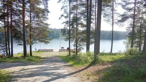 Un sentier de gravier mène à un banc situé au bord d’un lac, entouré de grands arbres.