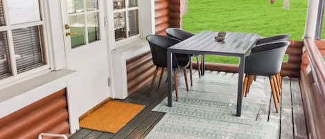 Un espacio al aire libre techado con mesa y sillas, una terraza de madera y vista a un jardín.