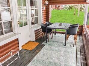Un espace extérieur abrité, doté d’une table et de chaises, d’une terrasse en bois et offrant une vue sur une pelouse.