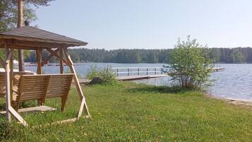A wooden gazebo with benches, a dock extending into a lake, and a forested shoreline.