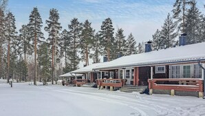 Un chalet enneigé, avec une façade en bois et une véranda couverte.