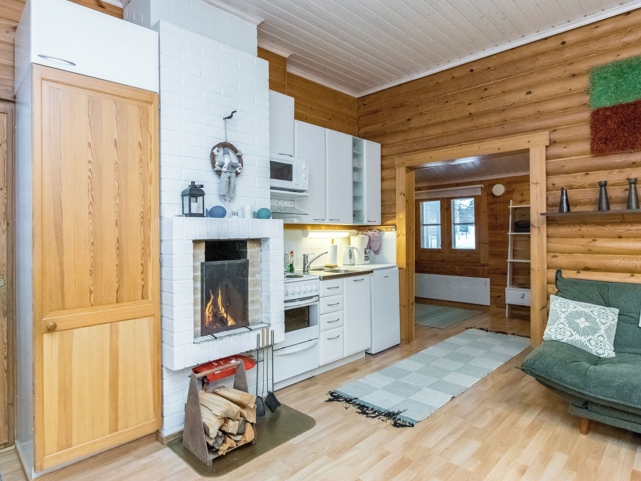 A cozy cabin interior with a fireplace, wooden walls, a kitchenette, and a green sofa.