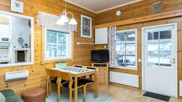 A cozy cabin interior with wooden walls, a fireplace, a dining table with chairs, a television, and a large window.