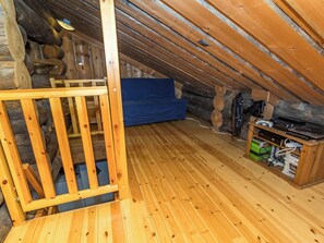 A wooden attic room with a sloped ceiling, a blue sofa, a wooden ladder, and a shelf with electronic devices. - Kelovalta 1b by Interhome (Kuusamo)