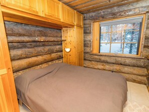 A log cabin room with a bed, a window with a view of a snowy forest, and a wall-mounted light fixture. - Kelovalta 1b by Interhome (Kuusamo)