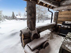A wooden cabin with a snow-covered porch, a grill, and a view of a snowy landscape. - Kelovalta 1b by Interhome (Kuusamo)