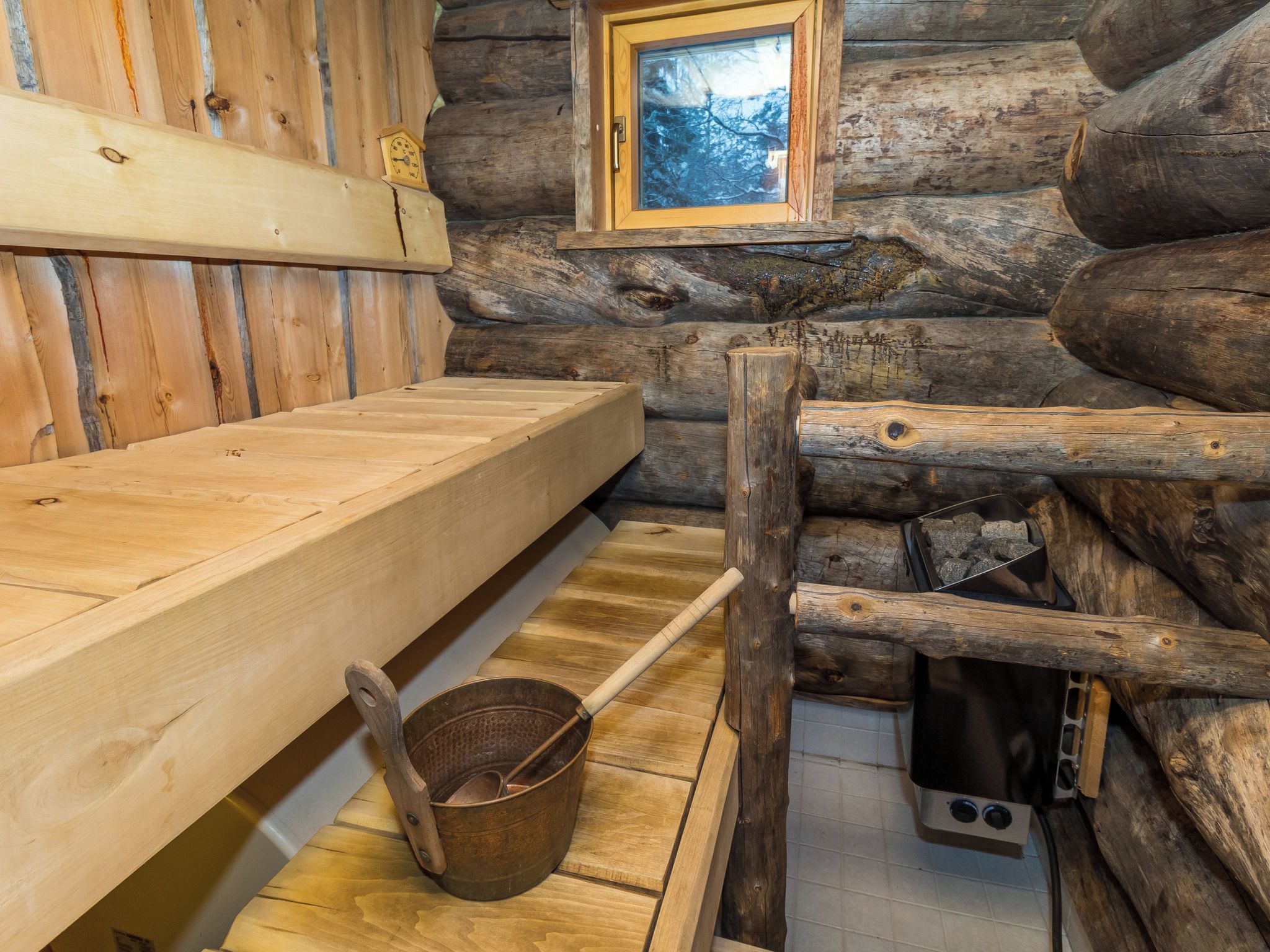 L’intérieur d’un chalet rustique en bois, avec un banc, un seau en bois et un poêle.
