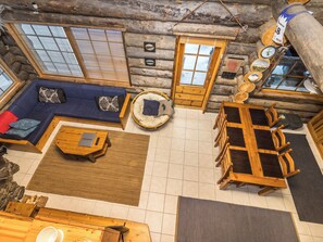 Interior de una cabaña de troncos con sofá, mesa redonda y comedor.