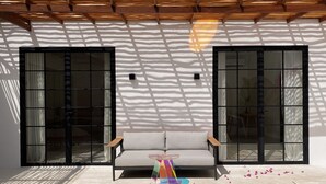 A modern outdoor seating area with a sofa and a colorful sculpture, surrounded by large windows and a wooden pergola.