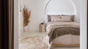 A bedroom with a bed, a bedside table, a lamp, and a decorative plant.