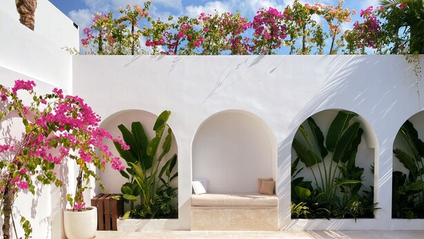 A pool area with a white wall, three arches, and potted plants.