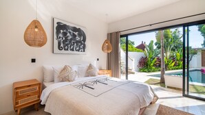 A bedroom with a large bed, two bedside tables, a wall-mounted artwork, and a view of a swimming pool and garden. - Private Pool | Rooftop Views | Canggu Base (Canggu)