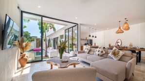 A modern living room with a sofa, coffee table, and a dining area with a table and chairs. - Private Pool | Rooftop Views | Canggu Base (Canggu)