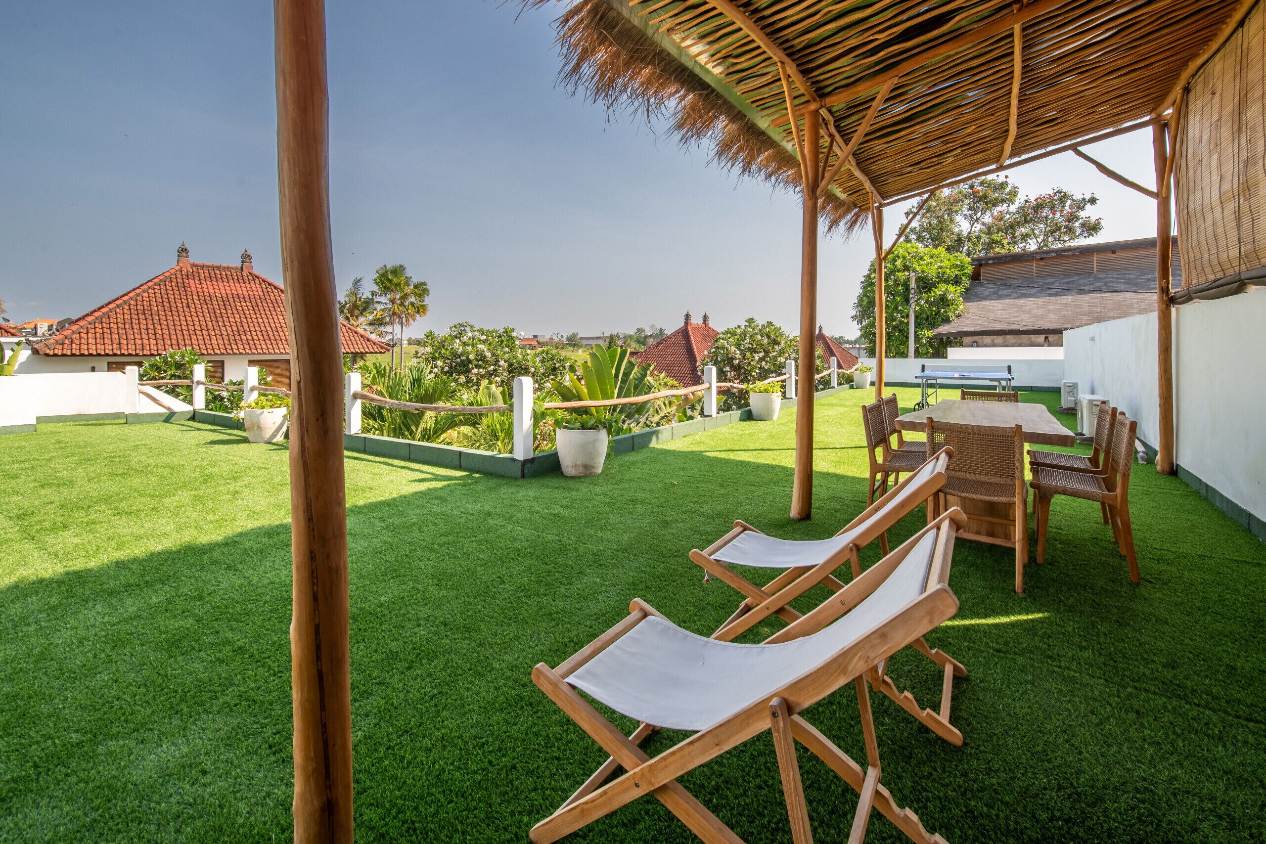 A covered outdoor area with artificial grass, wooden lounge chairs, and a table with chairs.