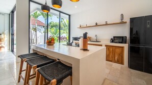 A modern kitchen with a large island, bar stools, a black refrigerator, and a view of the outdoors. - Private Pool | Rooftop Views | Canggu Base (Canggu)