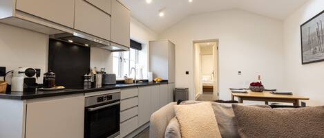 A modern kitchen with integrated appliances, a dining area with a table and chairs, and a cozy living space with a sofa and cushions.