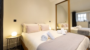 A hotel room with a large bed, a bedside table with a lamp, a mirror, and neatly folded towels. - The Bothy (Ulverston)