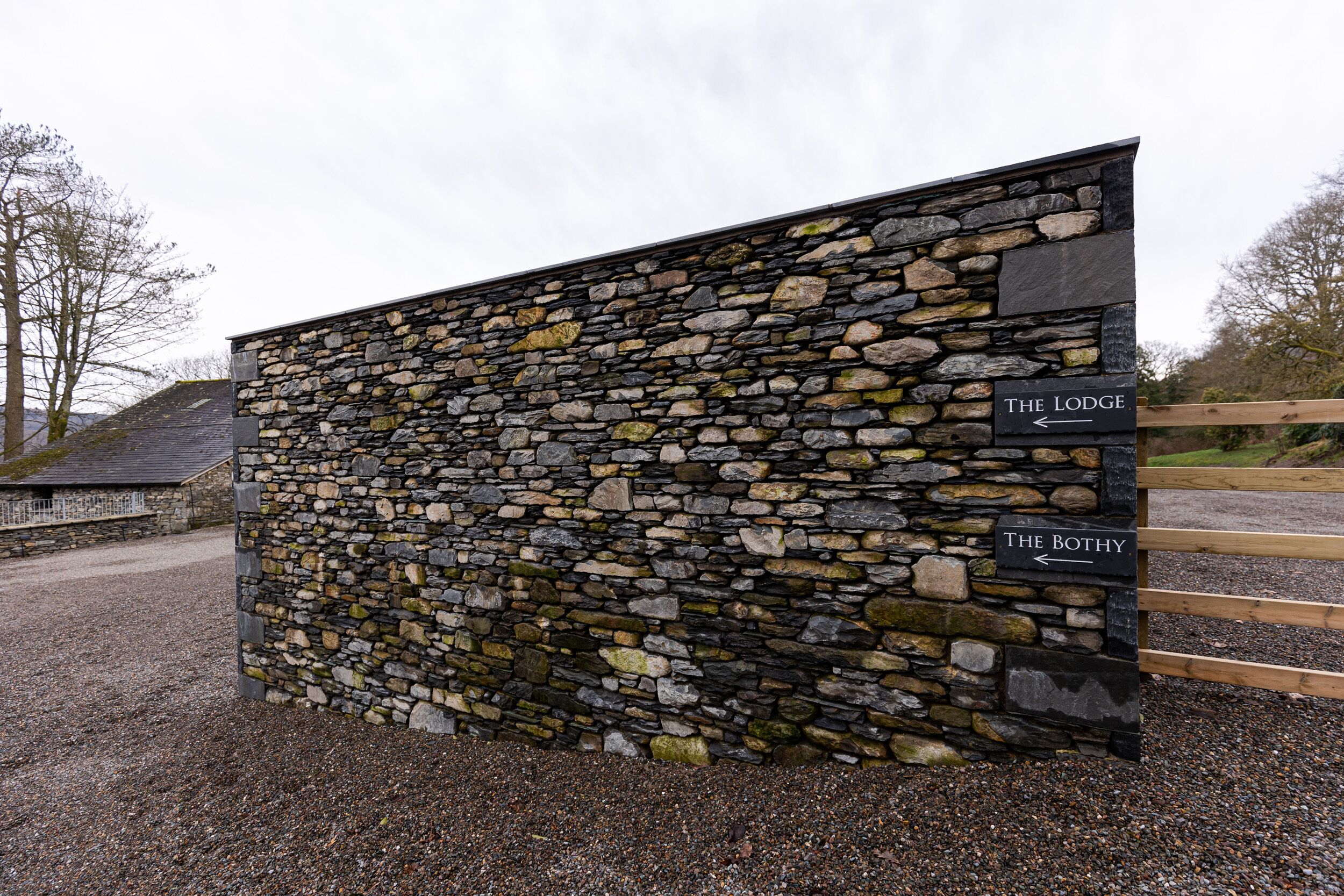 A stone wall with directional signs for 'The Lodge' and 'The Bothy'.